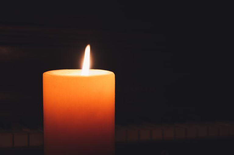 A single candle of remembrance glowing orange against a dark background
